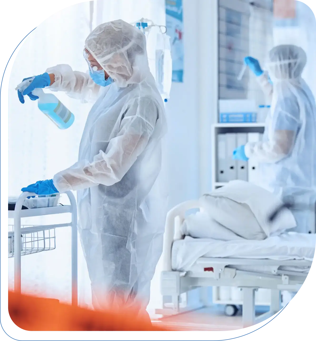 Healthcare workers in full protective gear spray disinfectant in a hospital room.